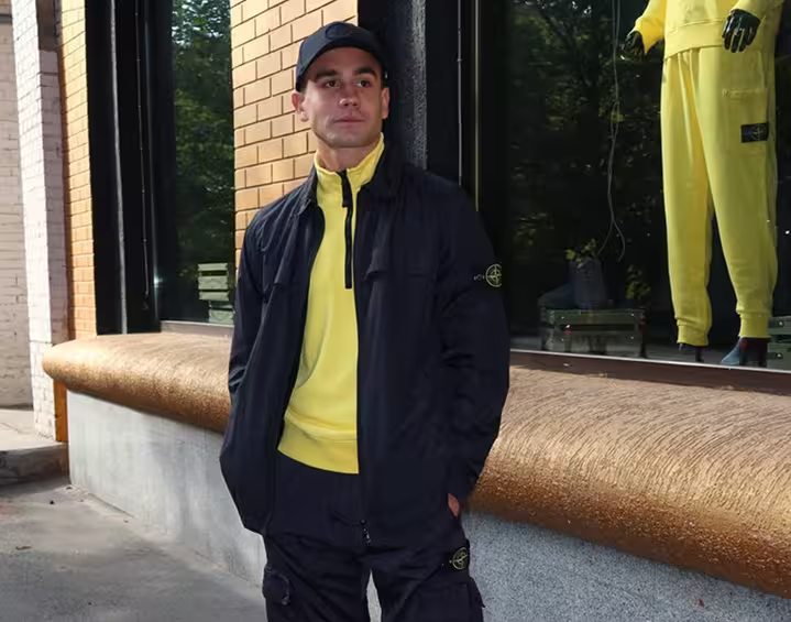 Man wearing black Stone Island outfit with yellow mid layer in urban style