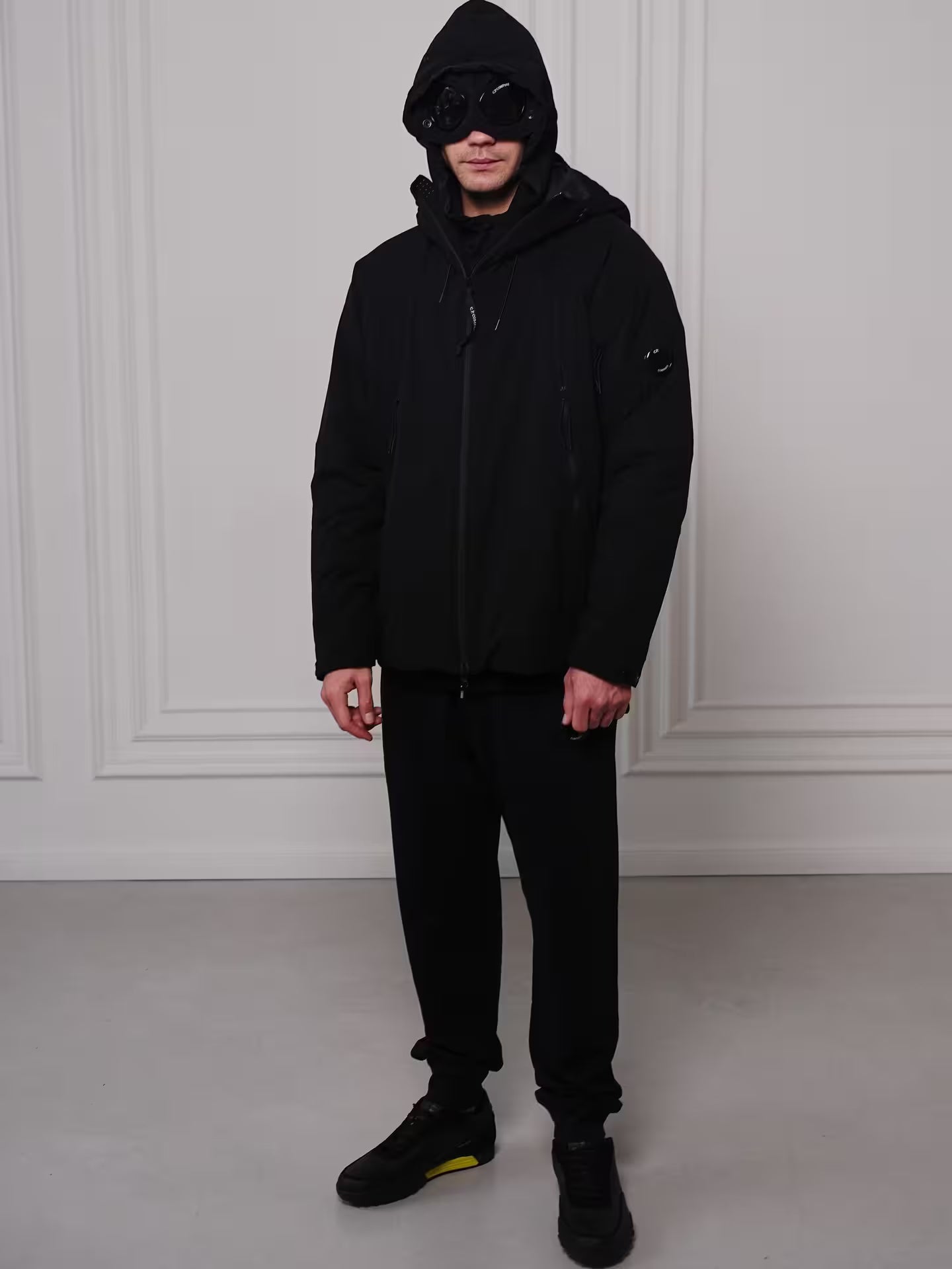 Man wearing black techwear hooded jacket with goggles in urban style