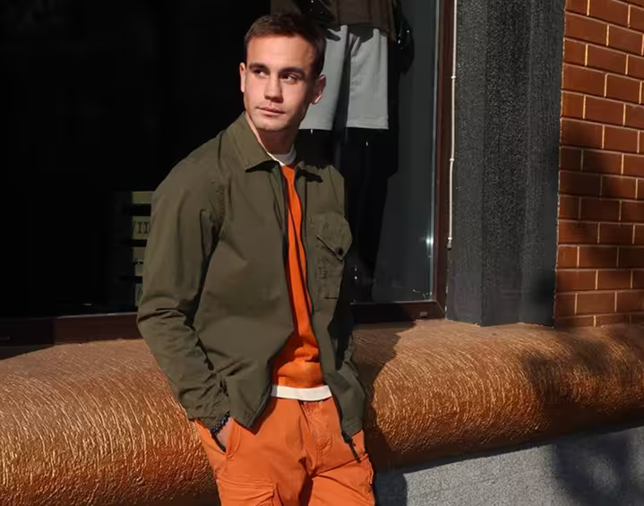 Man wearing olive jacket with orange streetwear outfit in urban setting